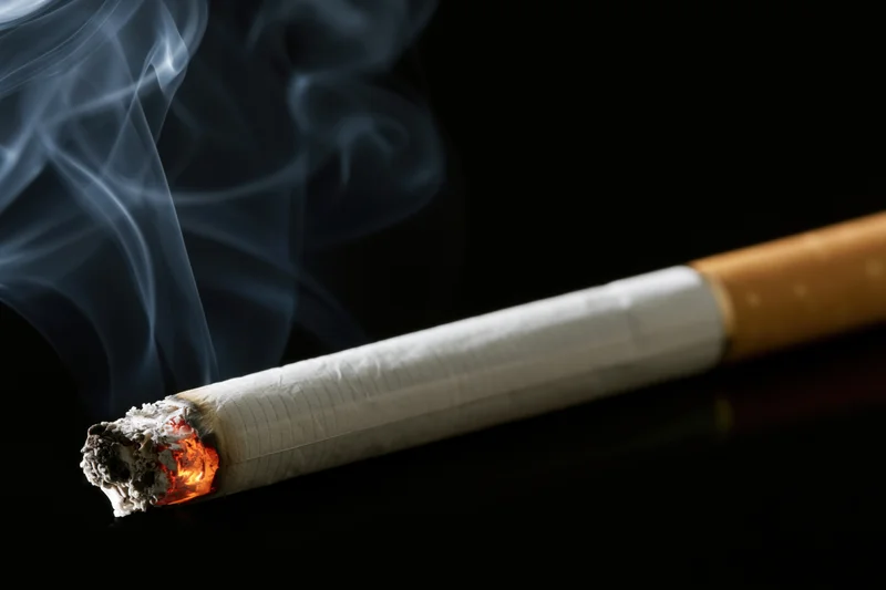Lit cigarette with glowing ember and rising smoke on black surface