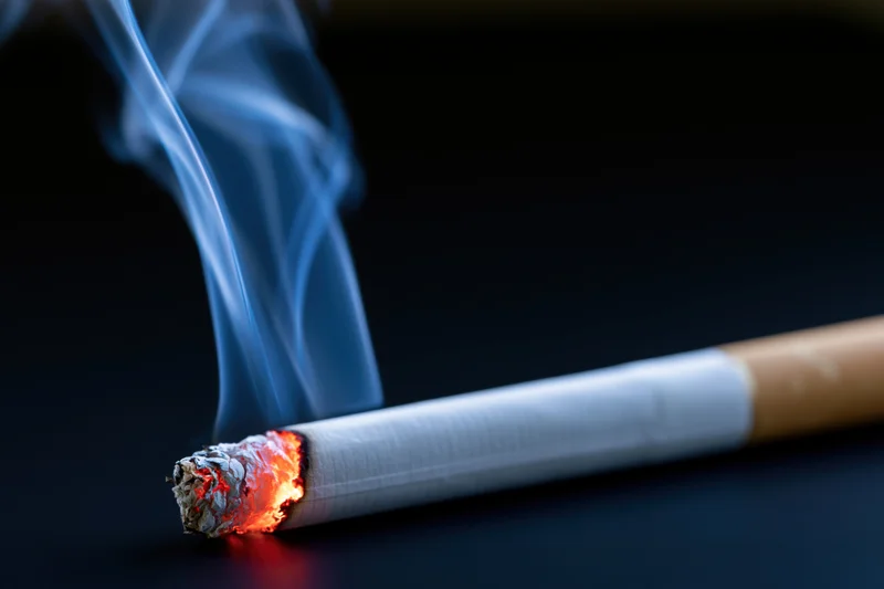 Lit cigarette burning with glowing ember and rising smoke on dark surface