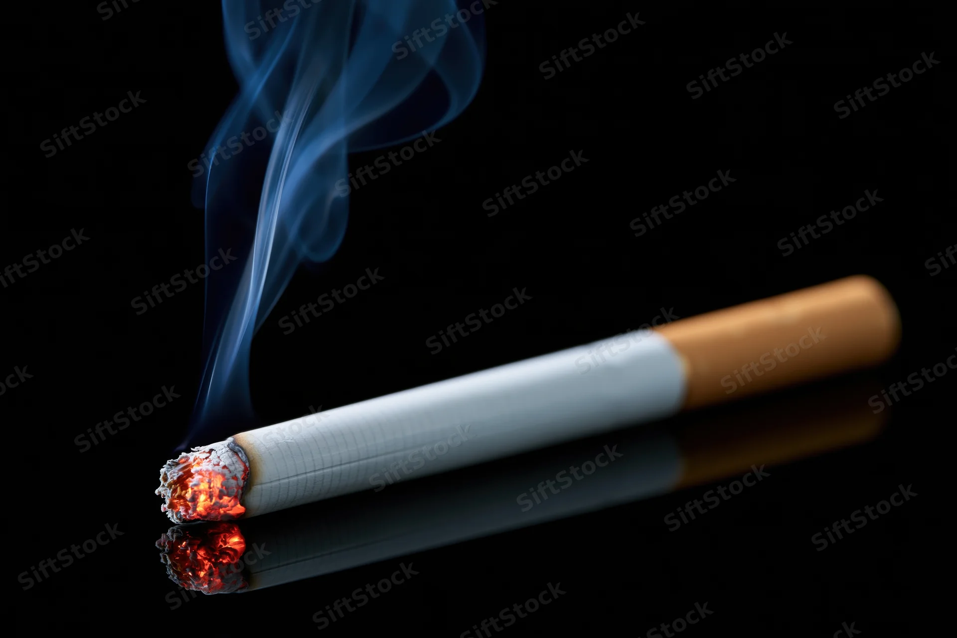 Lit cigarette burning horizontally on black reflective surface with smoke rising