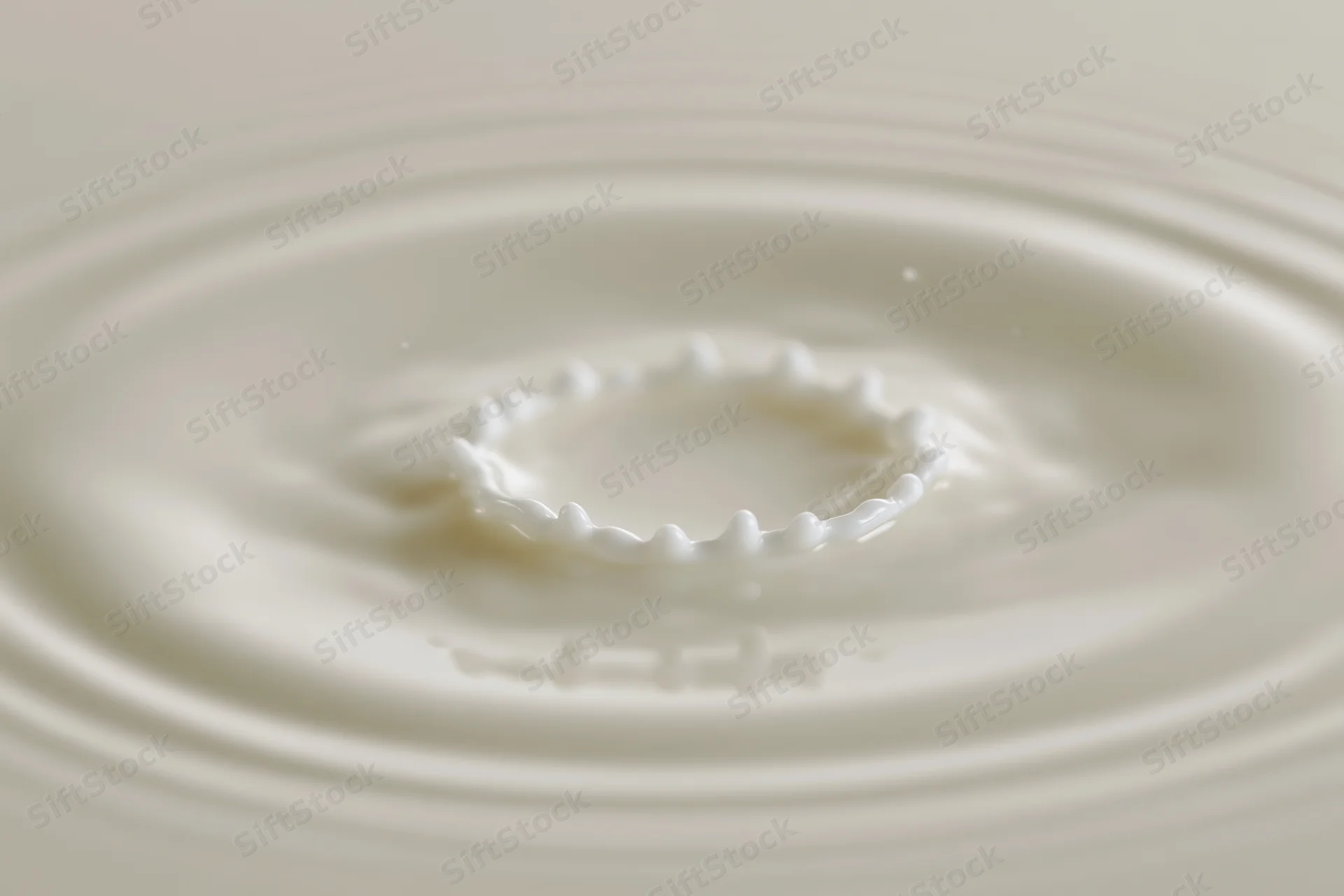 Milk drop creating crown splash on smooth surface with ripples spreading outward