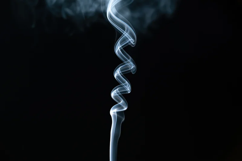 Thin white smoke rising in a spiral against a black background