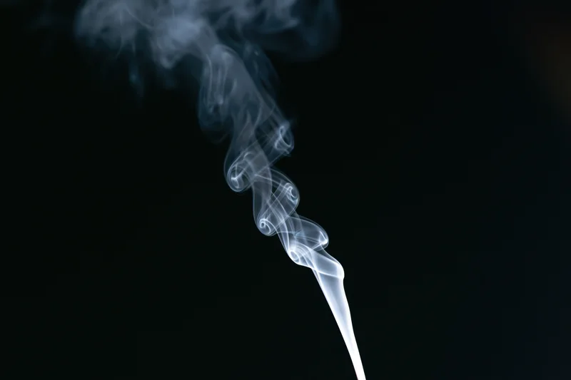 Thin wisp of white smoke rising and curling against black background