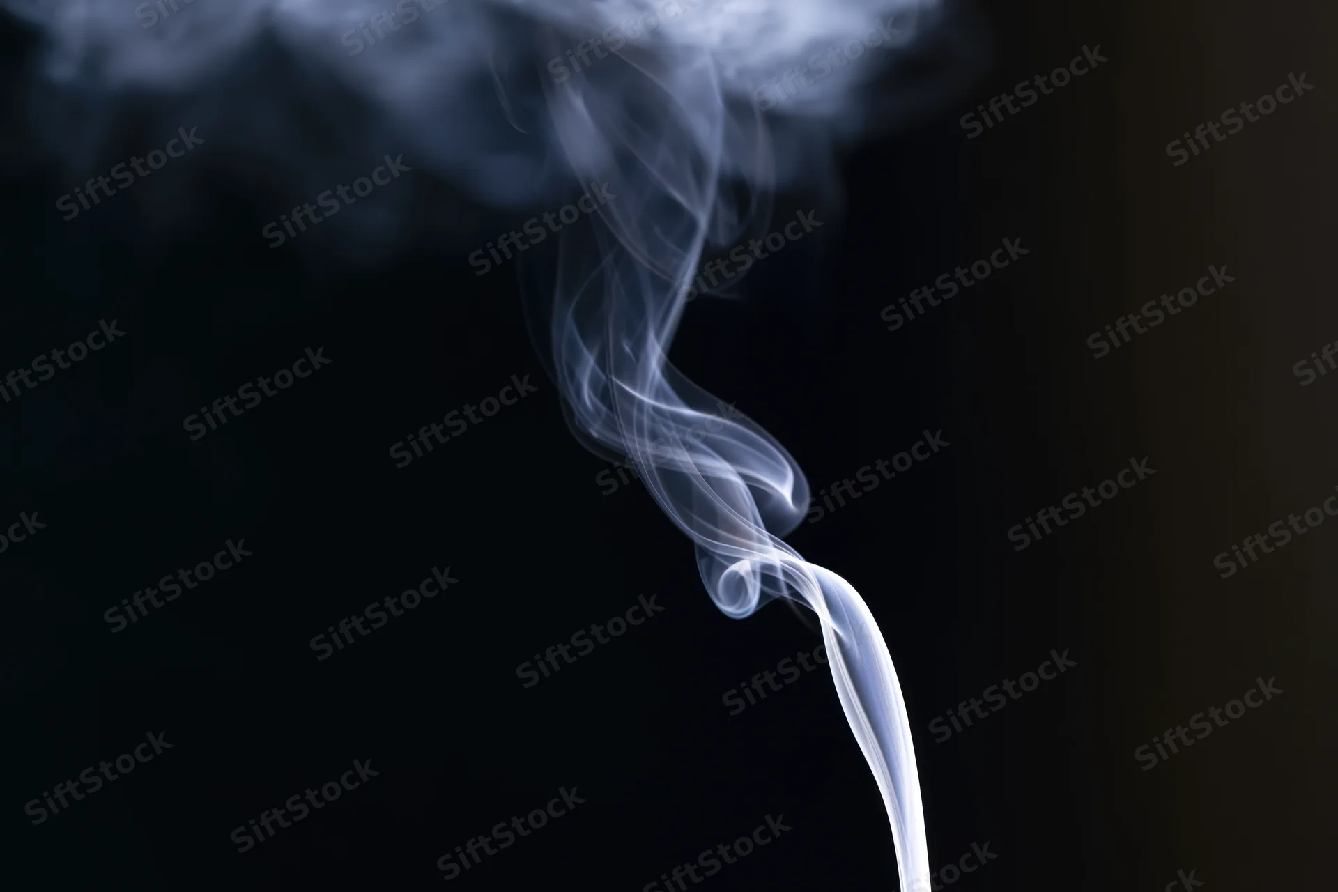 Thin wisp of white smoke rising and curling against dark background