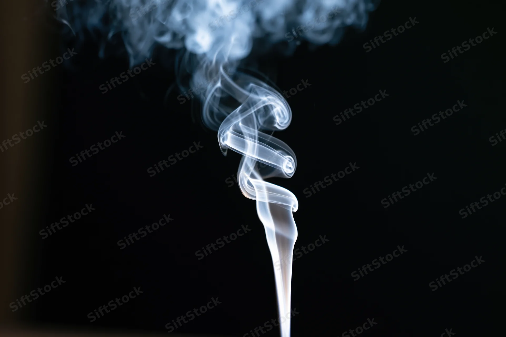 Thin wisp of white smoke rising and curling against black background