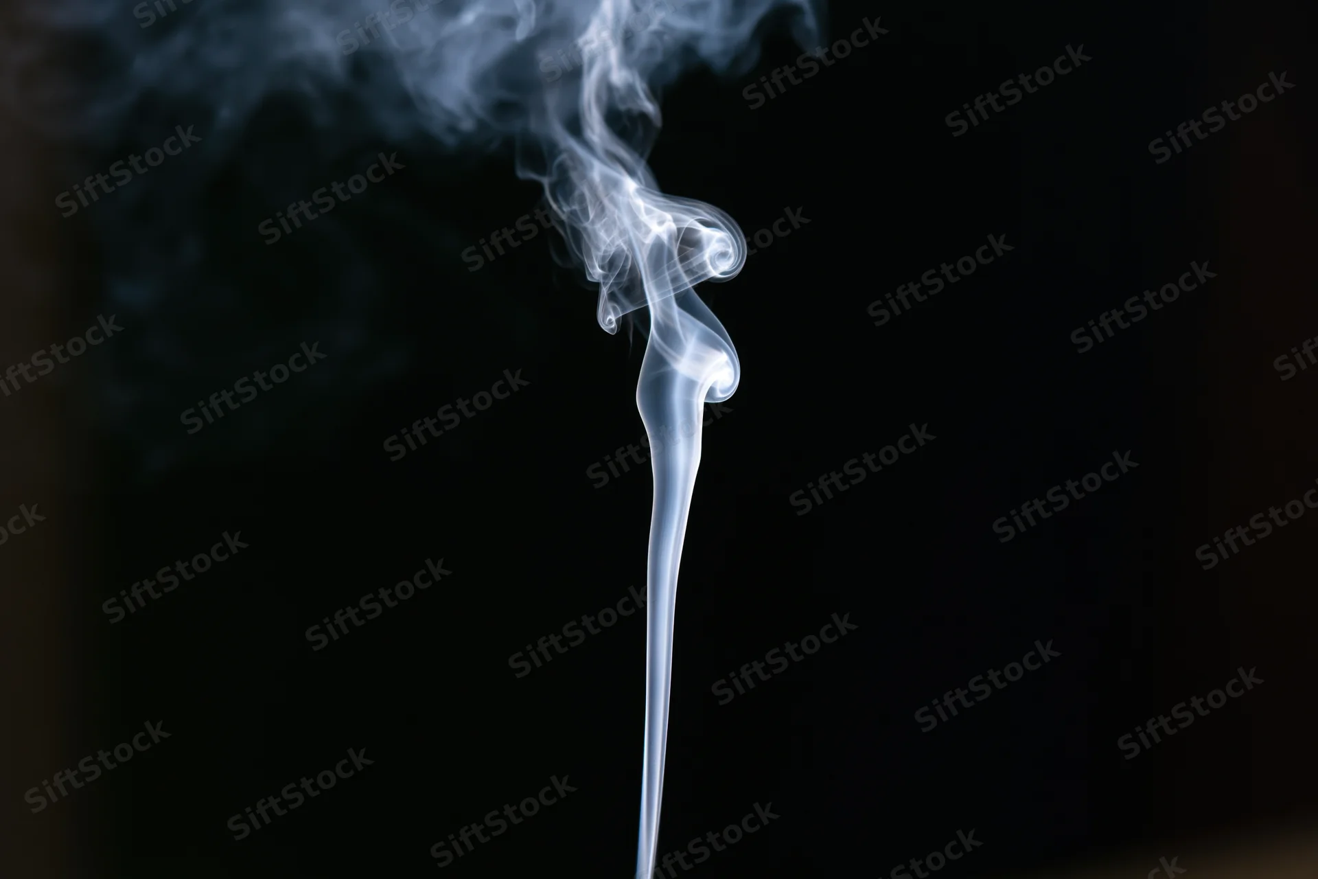 Thin wisp of white smoke rising and curling against black background