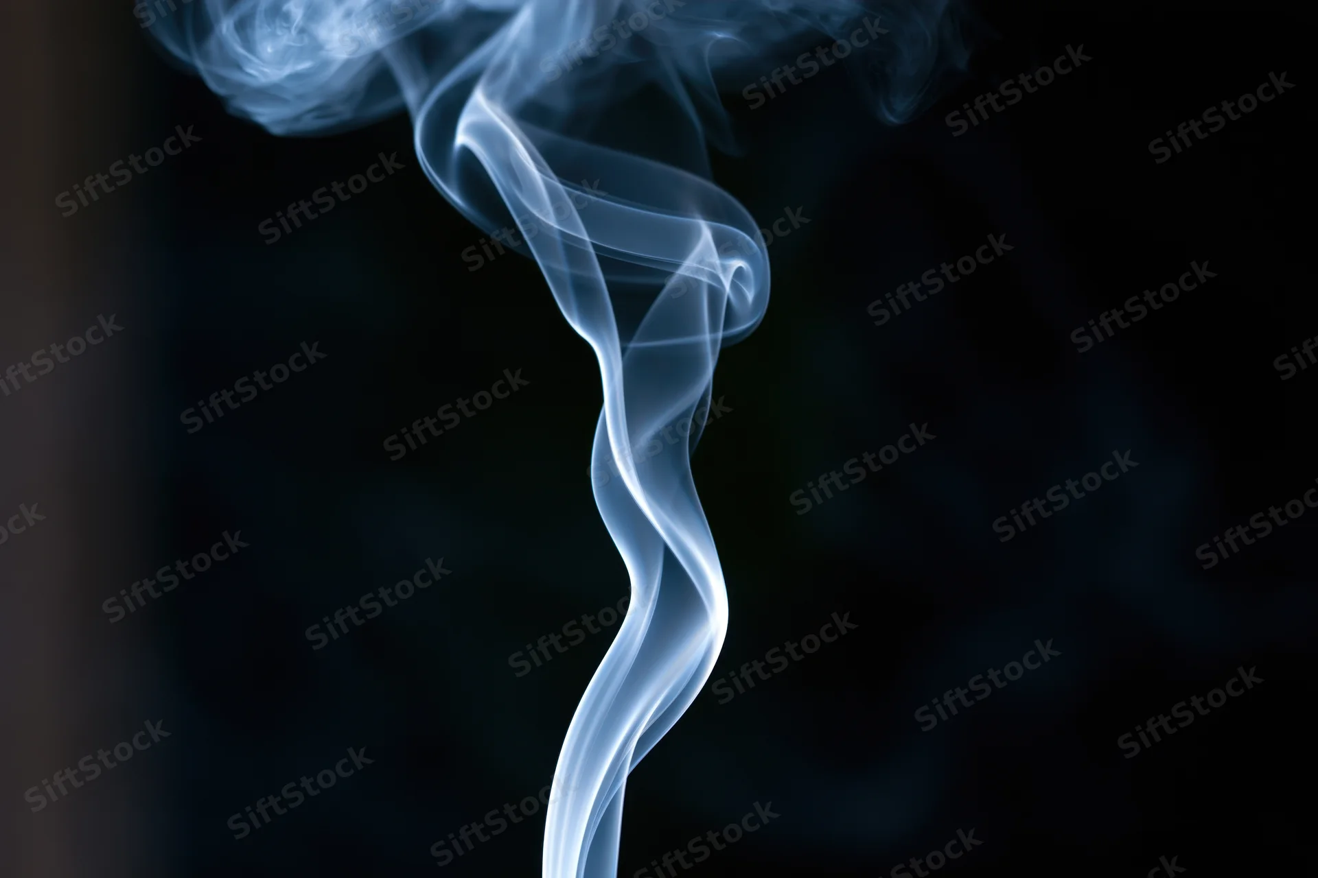 Thin wisp of white smoke rising and curling against dark background