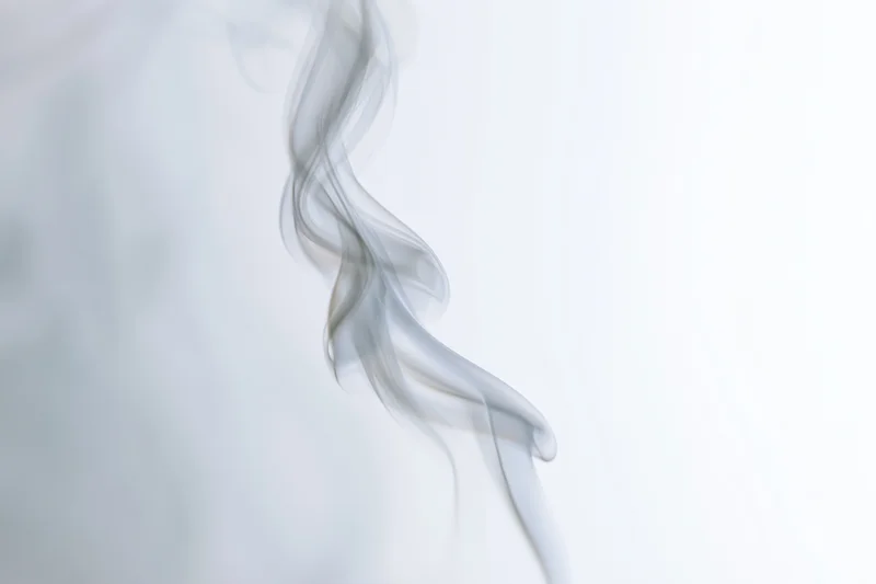 A single wisp of white smoke curling and twisting upward against a plain white background