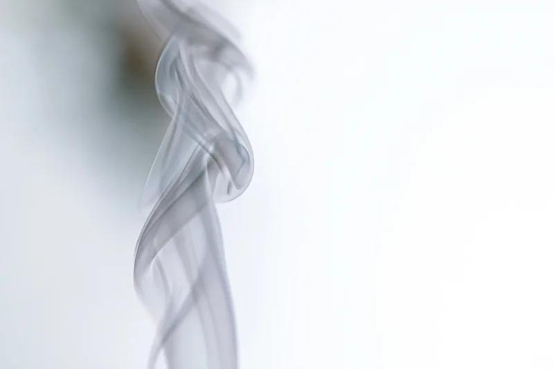 A single wisp of white smoke curling and twisting upward against a bright background