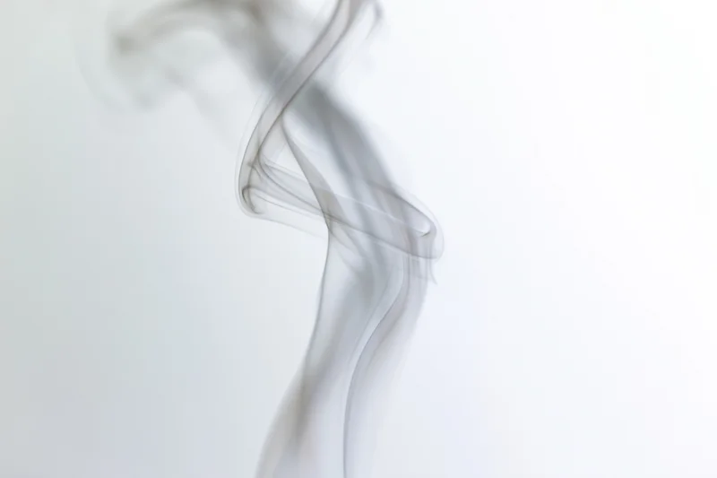 A single wisp of white smoke curling and twisting upward against a plain white background