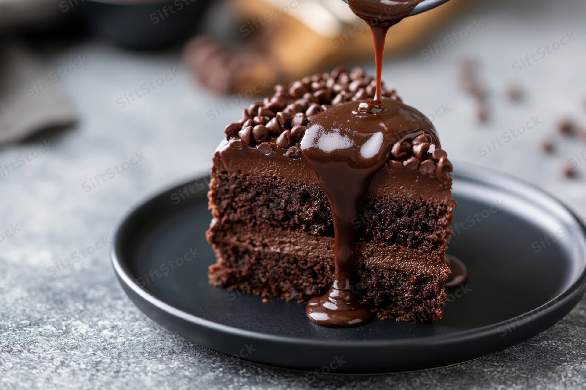 Slice of dark chocolate layer cake on matte black plate with chocolate syrup being poured over it