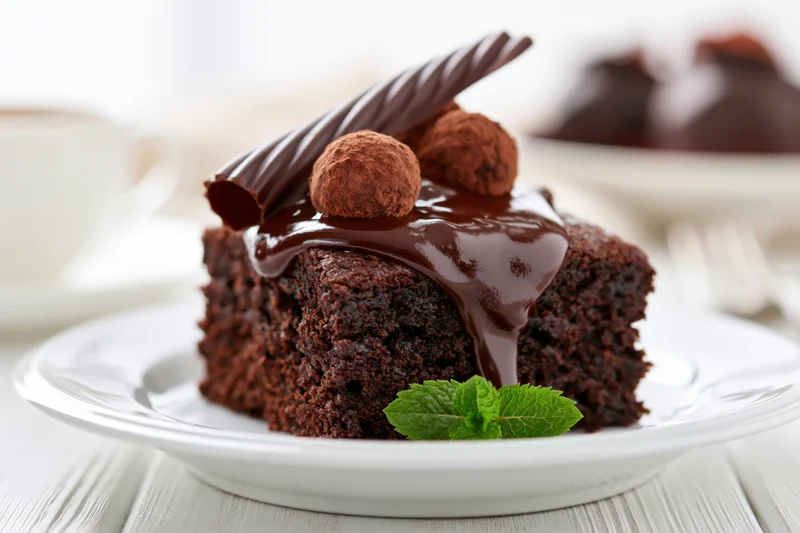 Slice of dense chocolate brownie cake topped with warm ganache