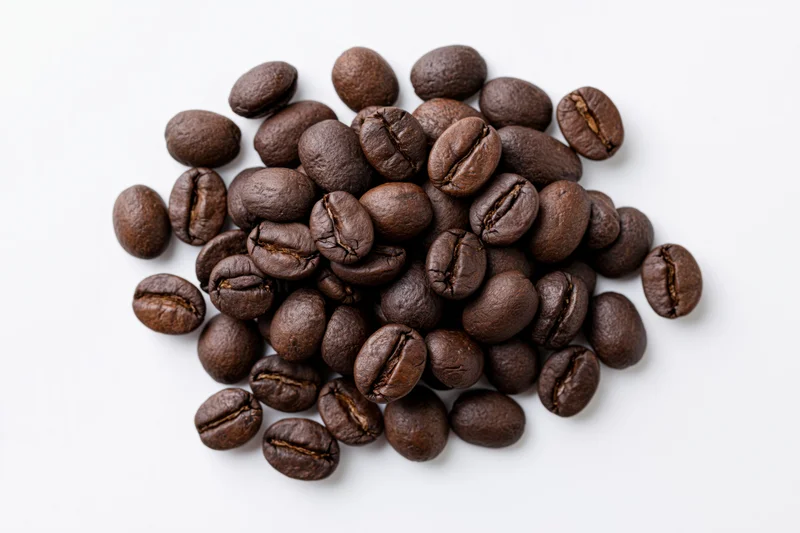 Dark roasted coffee beans scattered in a loose pile on white background
