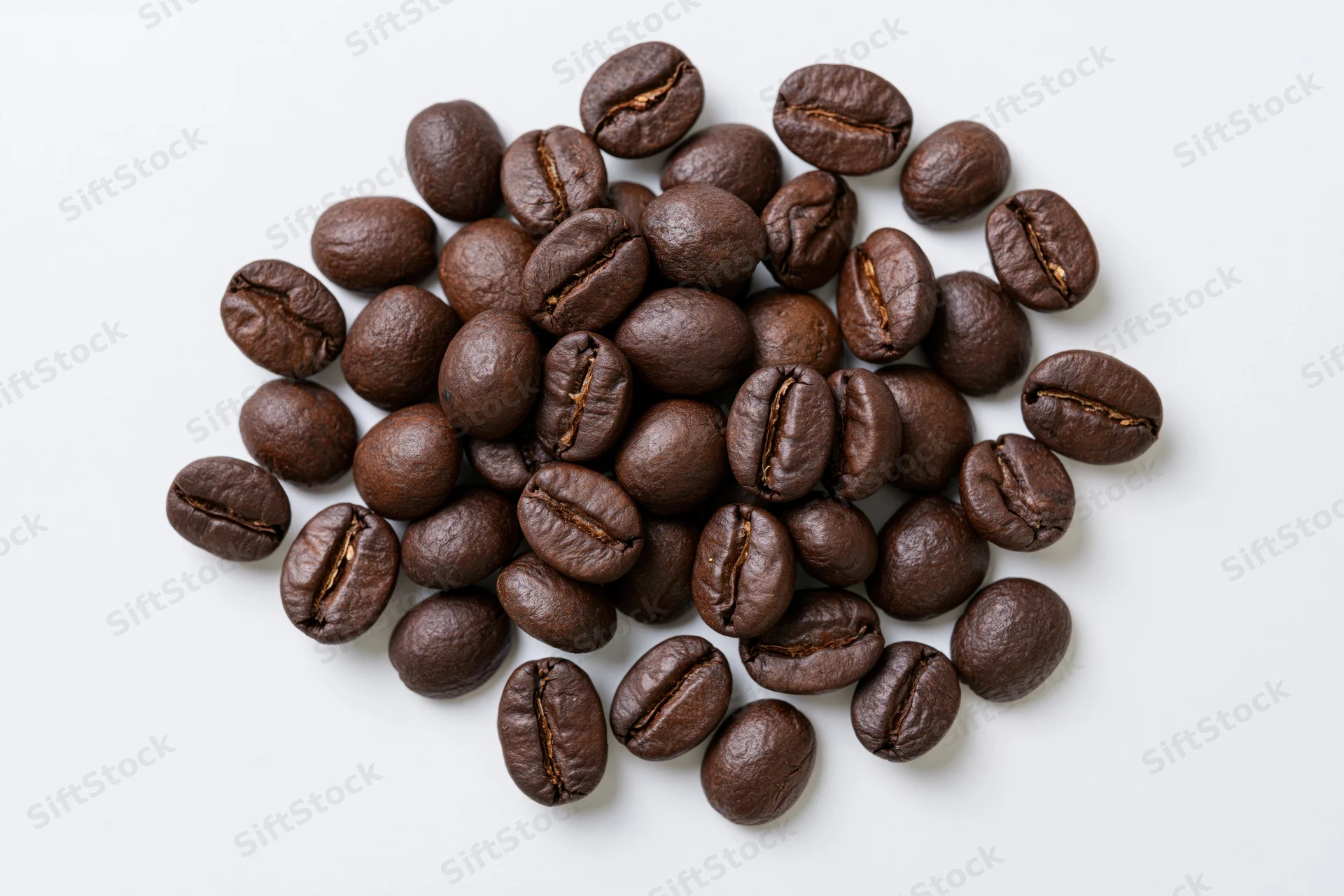 Dark roasted coffee beans scattered in a loose pile on white background