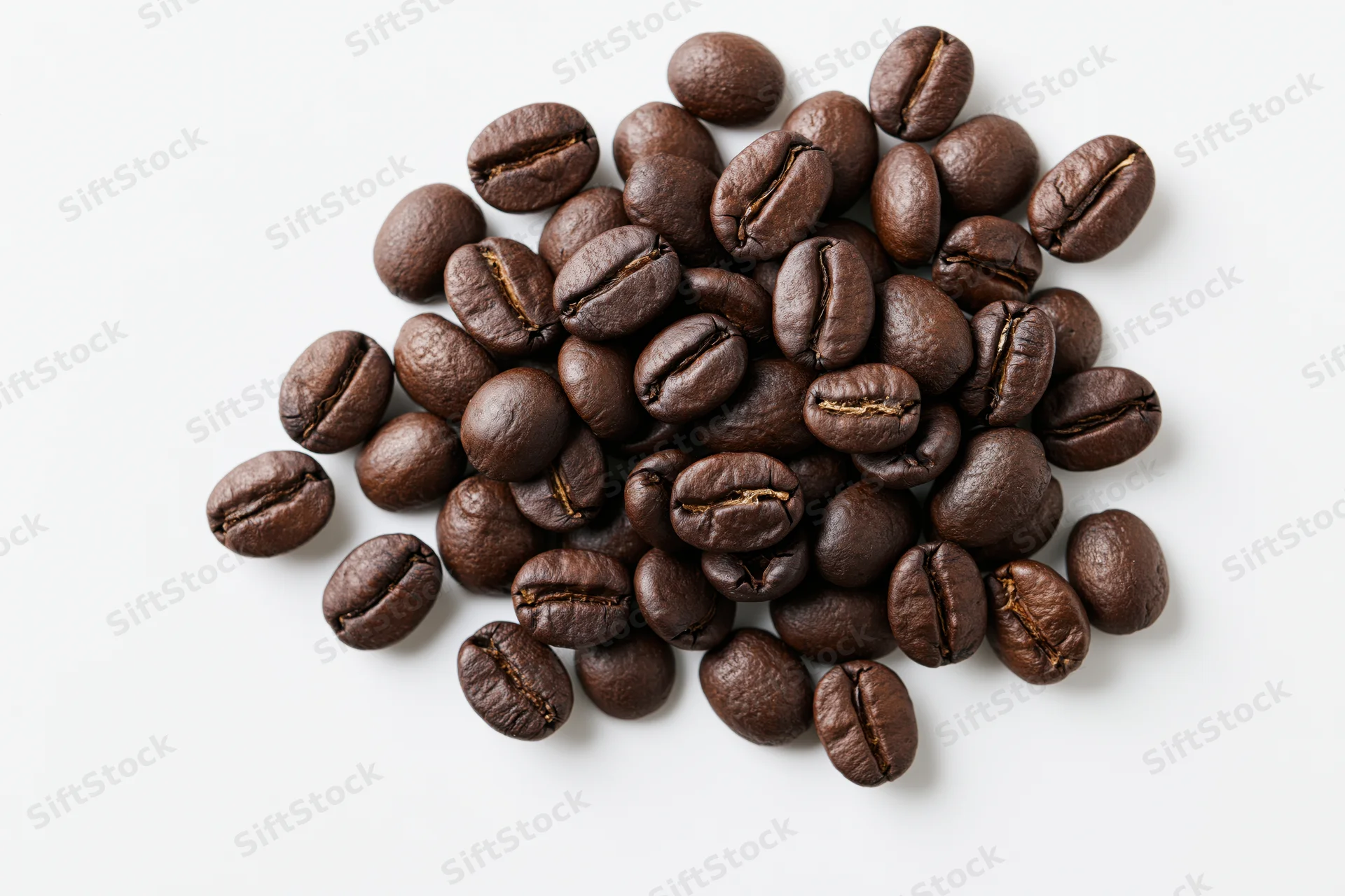 Dark roasted coffee beans scattered in a small pile on white background