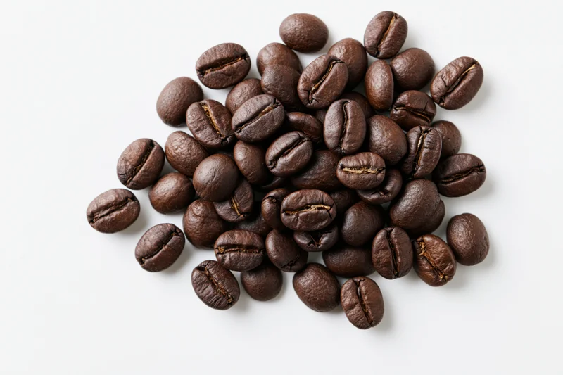 Dark roasted coffee beans scattered in a small pile on white background