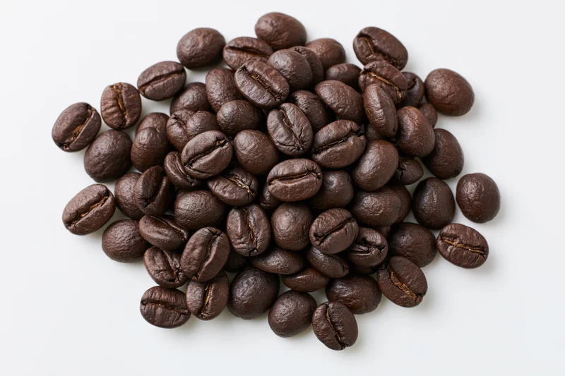 Dark roasted coffee beans scattered in a loose pile on white background