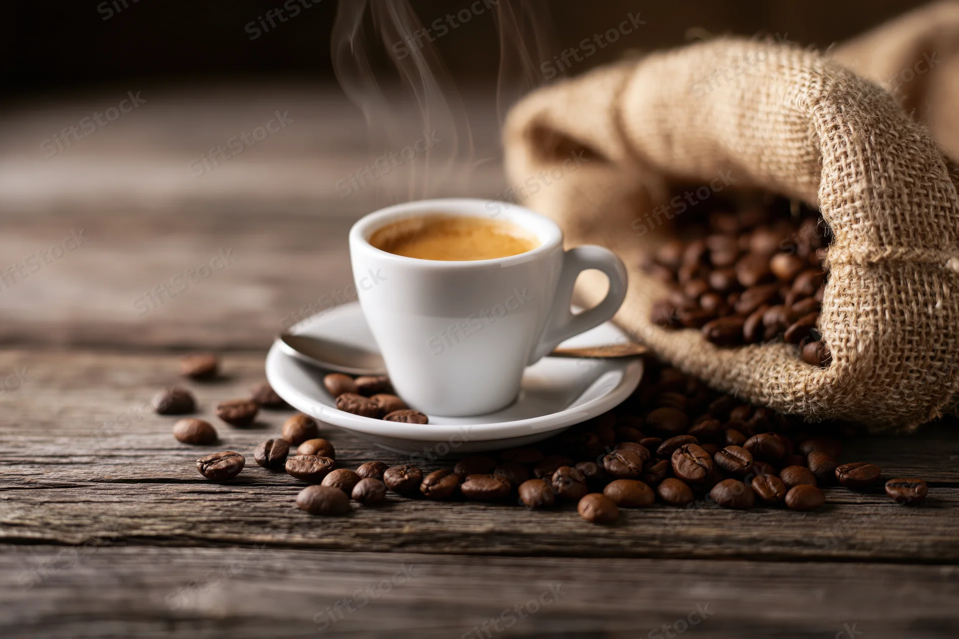 Steaming espresso cup with crema on saucer beside burlap sack of coffee beans on wooden table