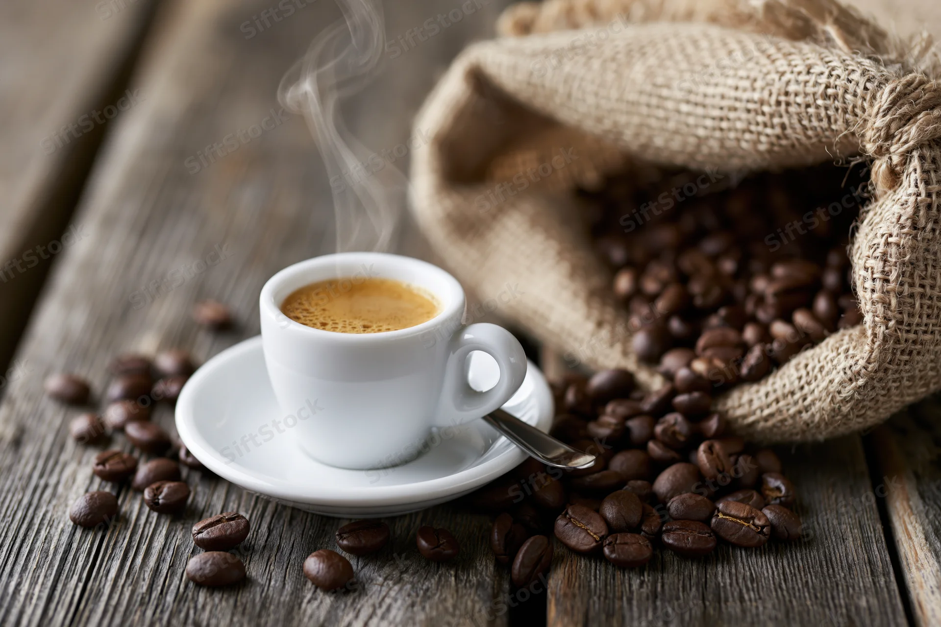 Steaming espresso cup with crema on saucer beside burlap sack of coffee beans on wooden table