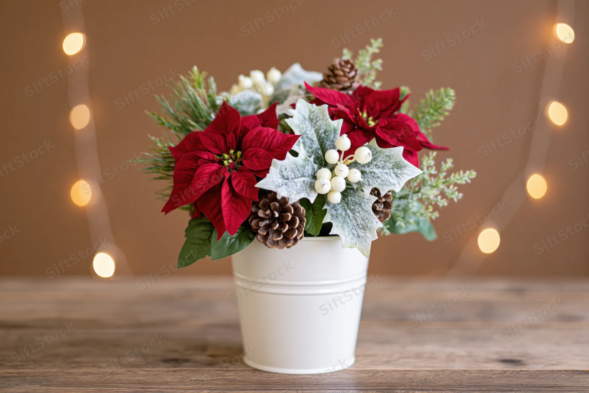 Christmas floral arrangement in white metal bucket on wooden table with string lights in background