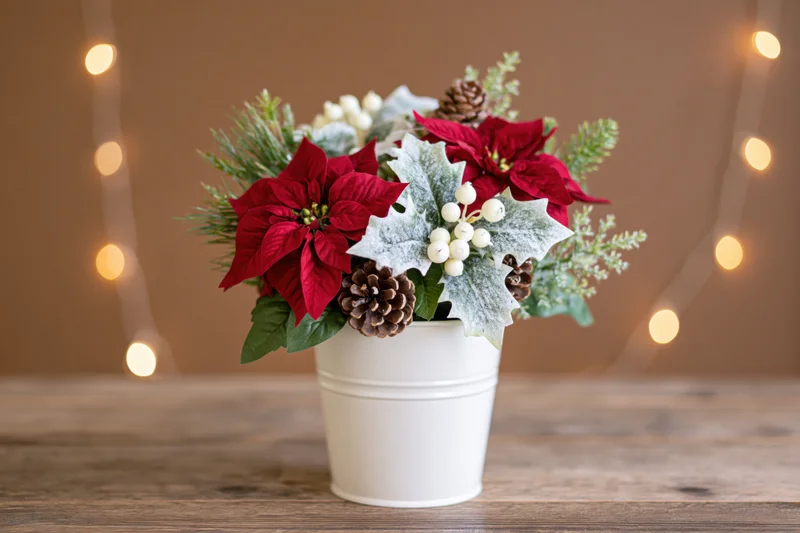 Christmas floral arrangement in white metal bucket on wooden table with string lights in background