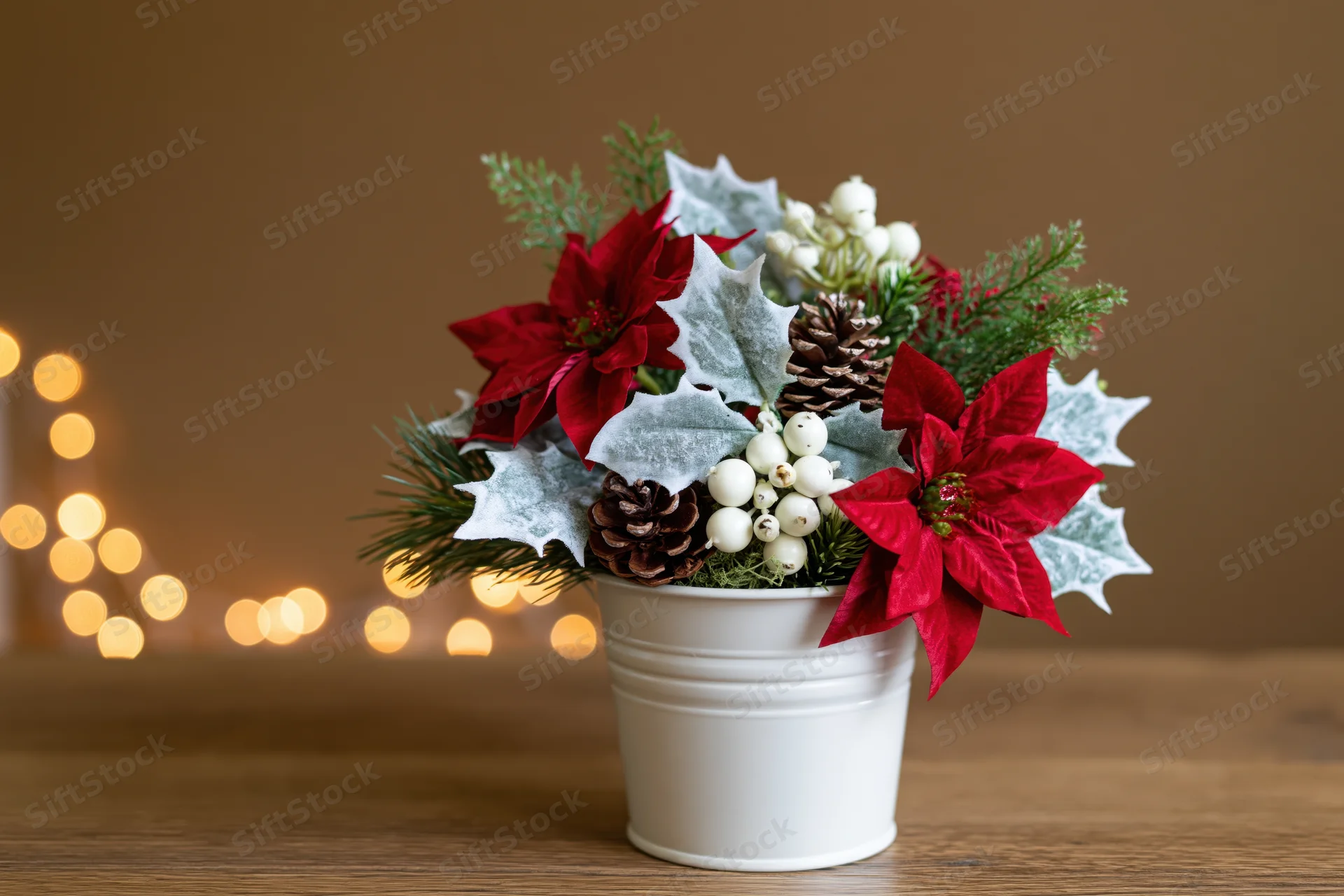 Christmas floral arrangement in a white metal bucket on a wooden table with blurred lights in the background
