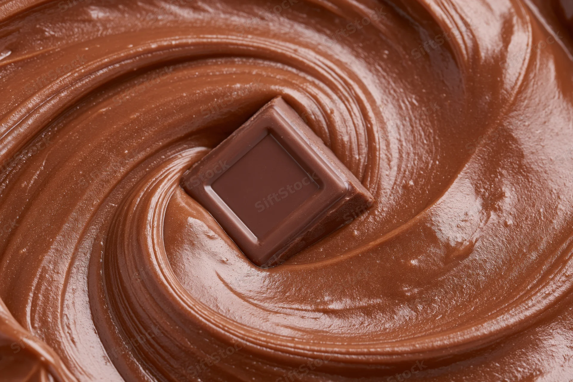 Chocolate square partially submerged in swirling melted chocolate
