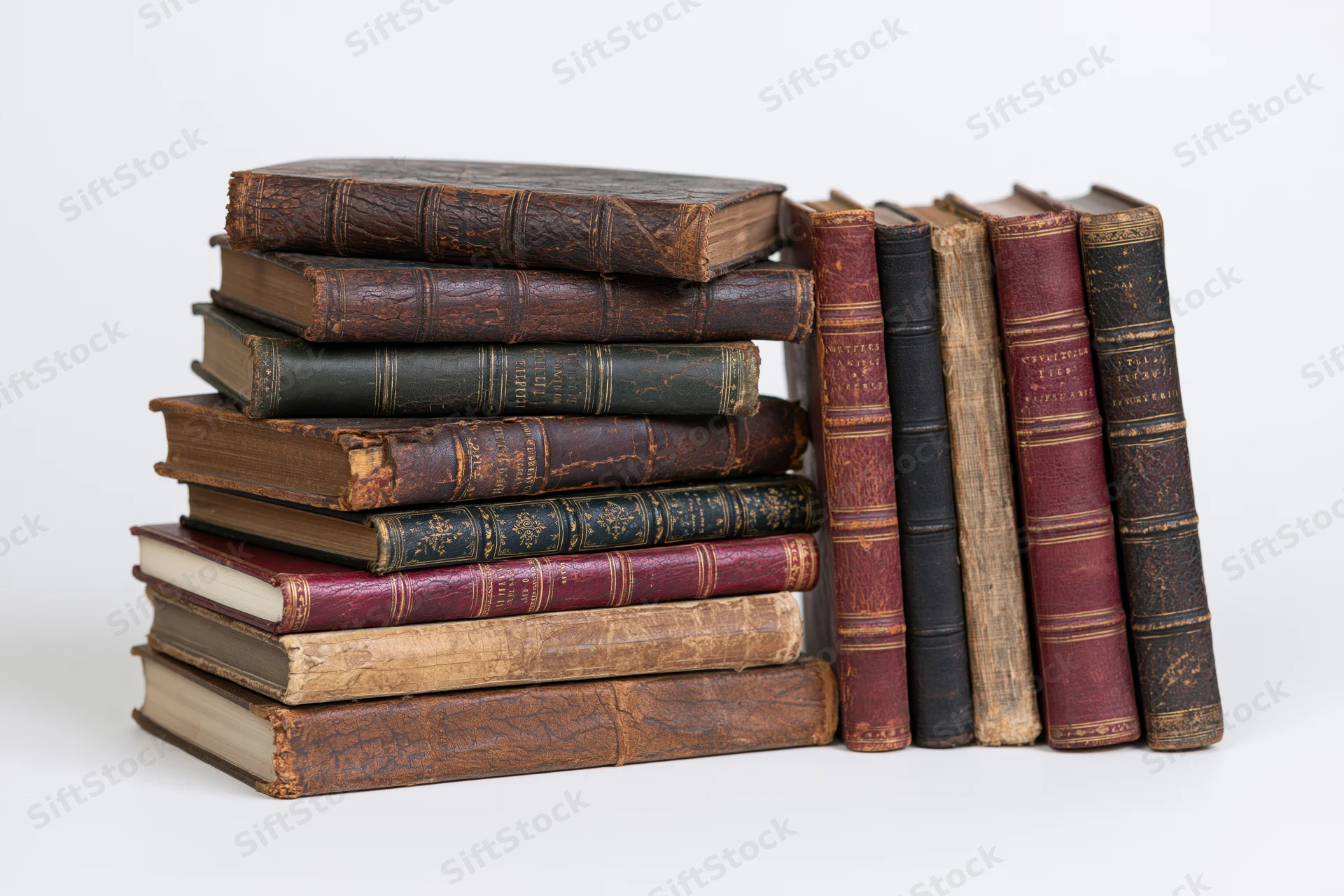 Stack of worn antique leather-bound books arranged vertically and horizontally on white background