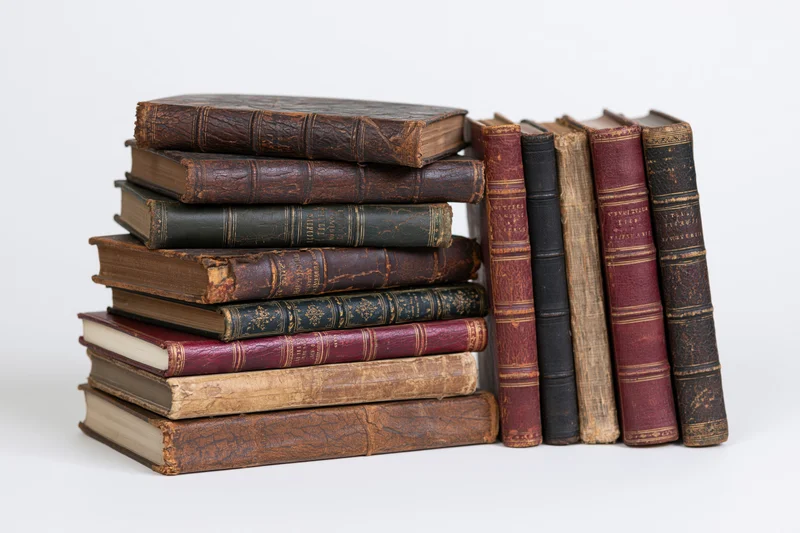 Stack of worn antique leather-bound books arranged vertically and horizontally on white background