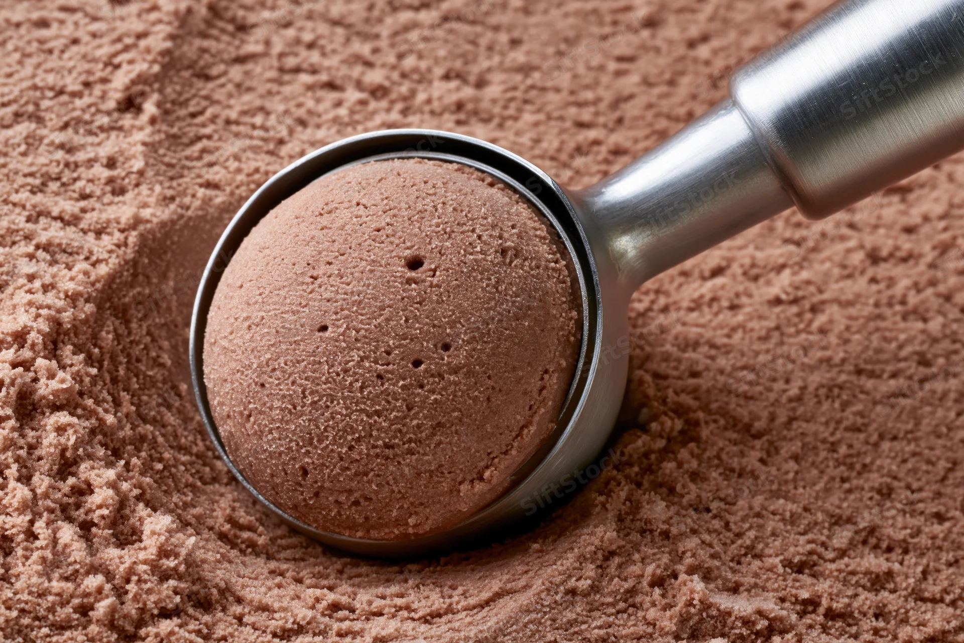 Stainless steel scoop lifting a rounded ball of cocoa powder from a pile