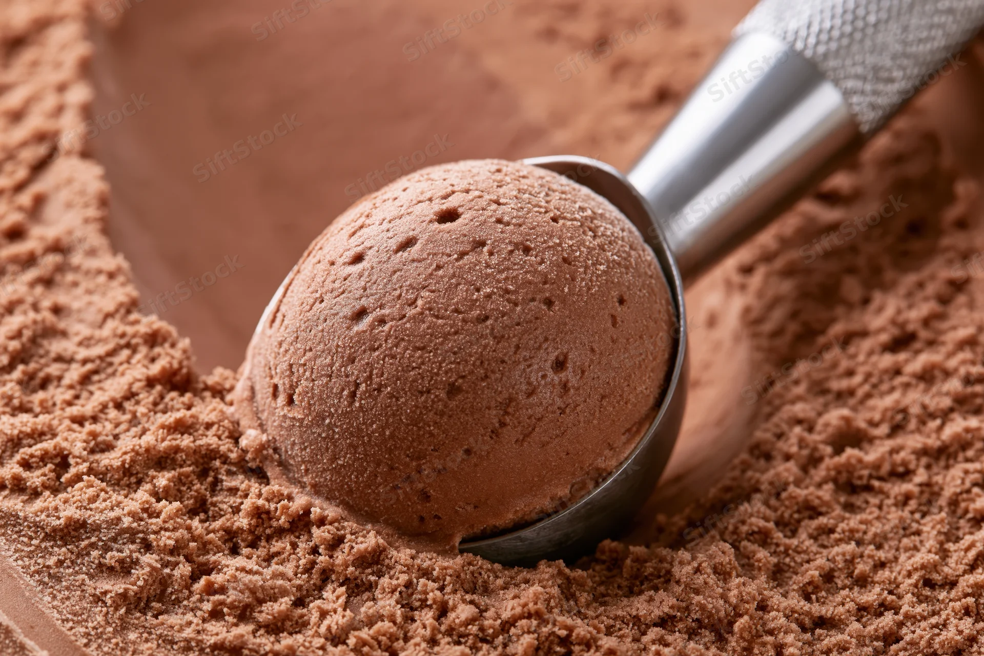 Stainless steel ice cream scoop lifting a rounded ball of chocolate ice cream from cocoa powder