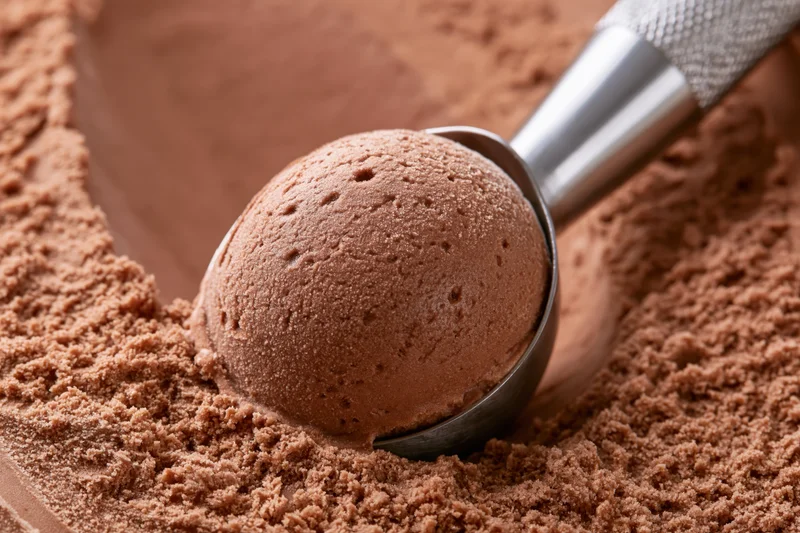 Stainless steel ice cream scoop lifting a rounded ball of chocolate ice cream from cocoa powder