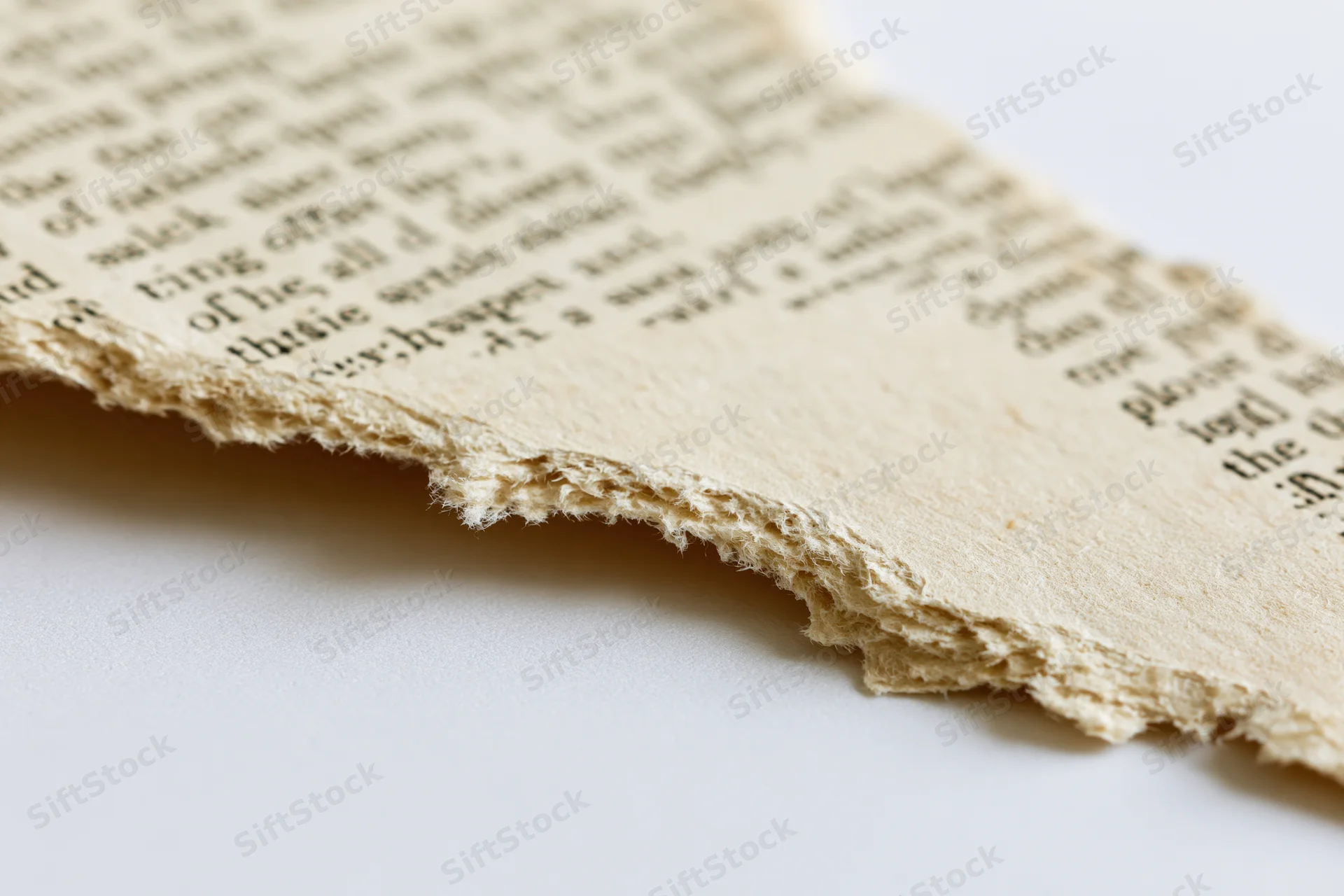 Torn fragment of aged paperback novel page with ragged edge on white background