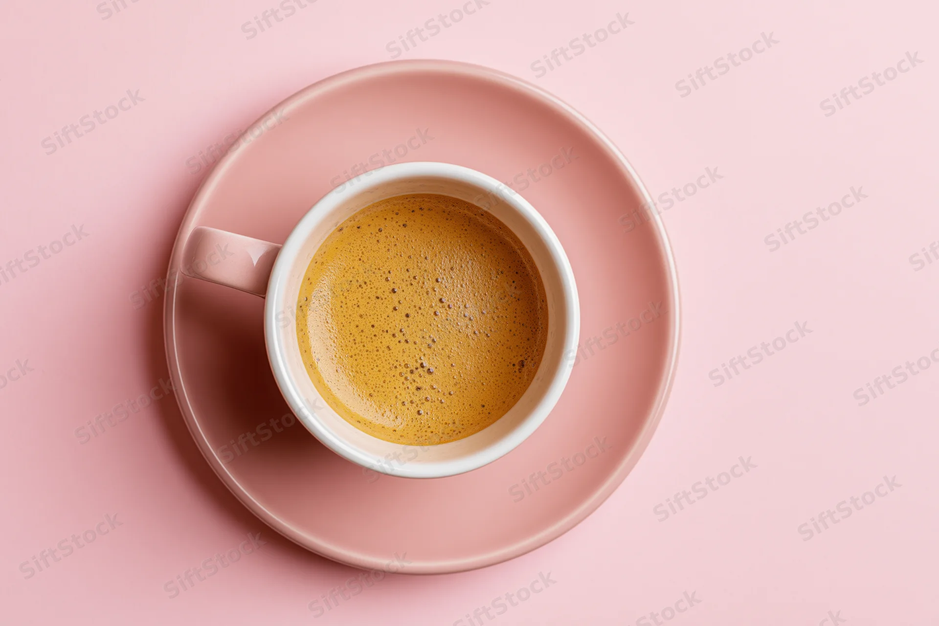 White ceramic coffee cup with frothy espresso on pink saucer, overhead view