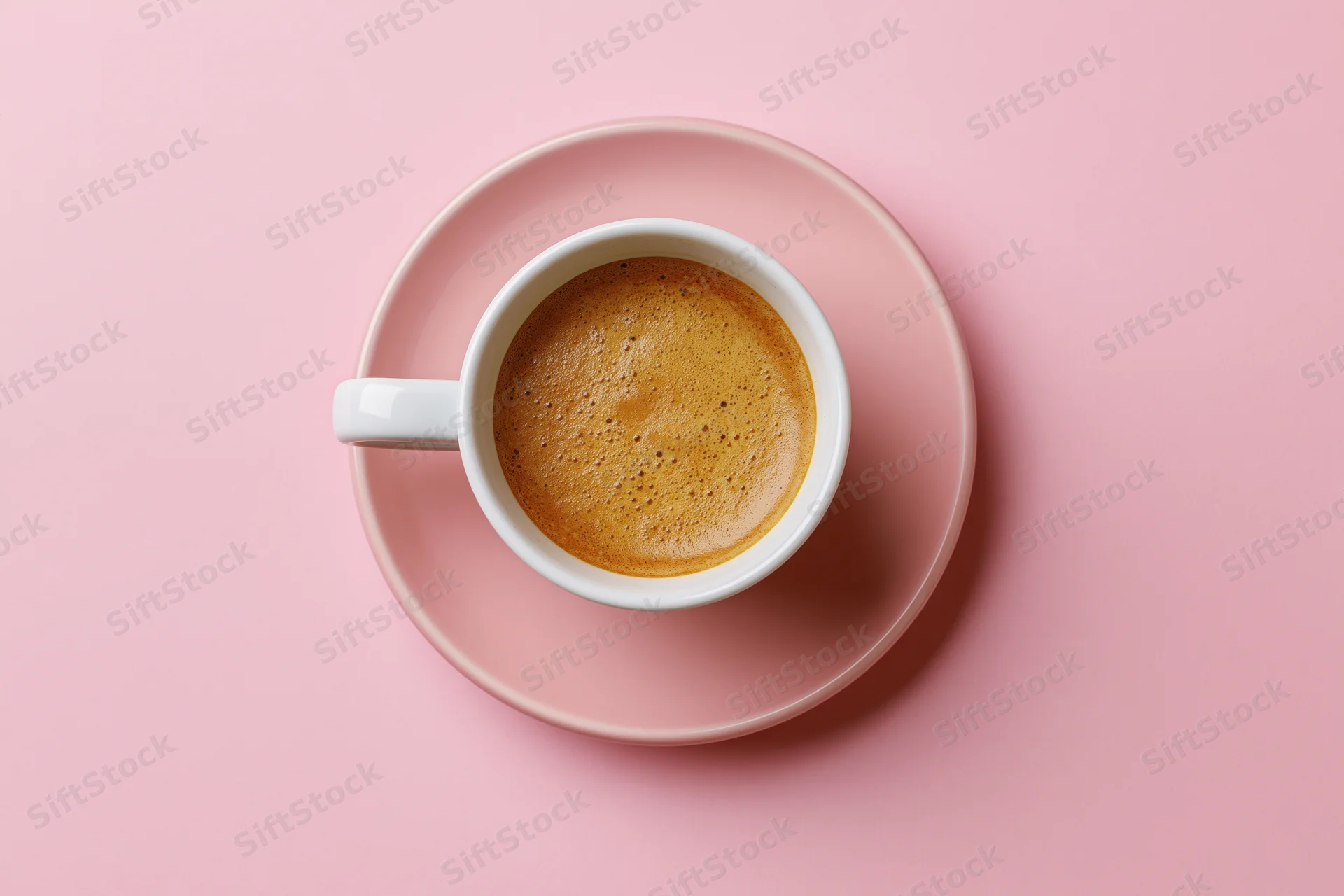 White ceramic coffee cup with frothy espresso on pink saucer, top view flat lay