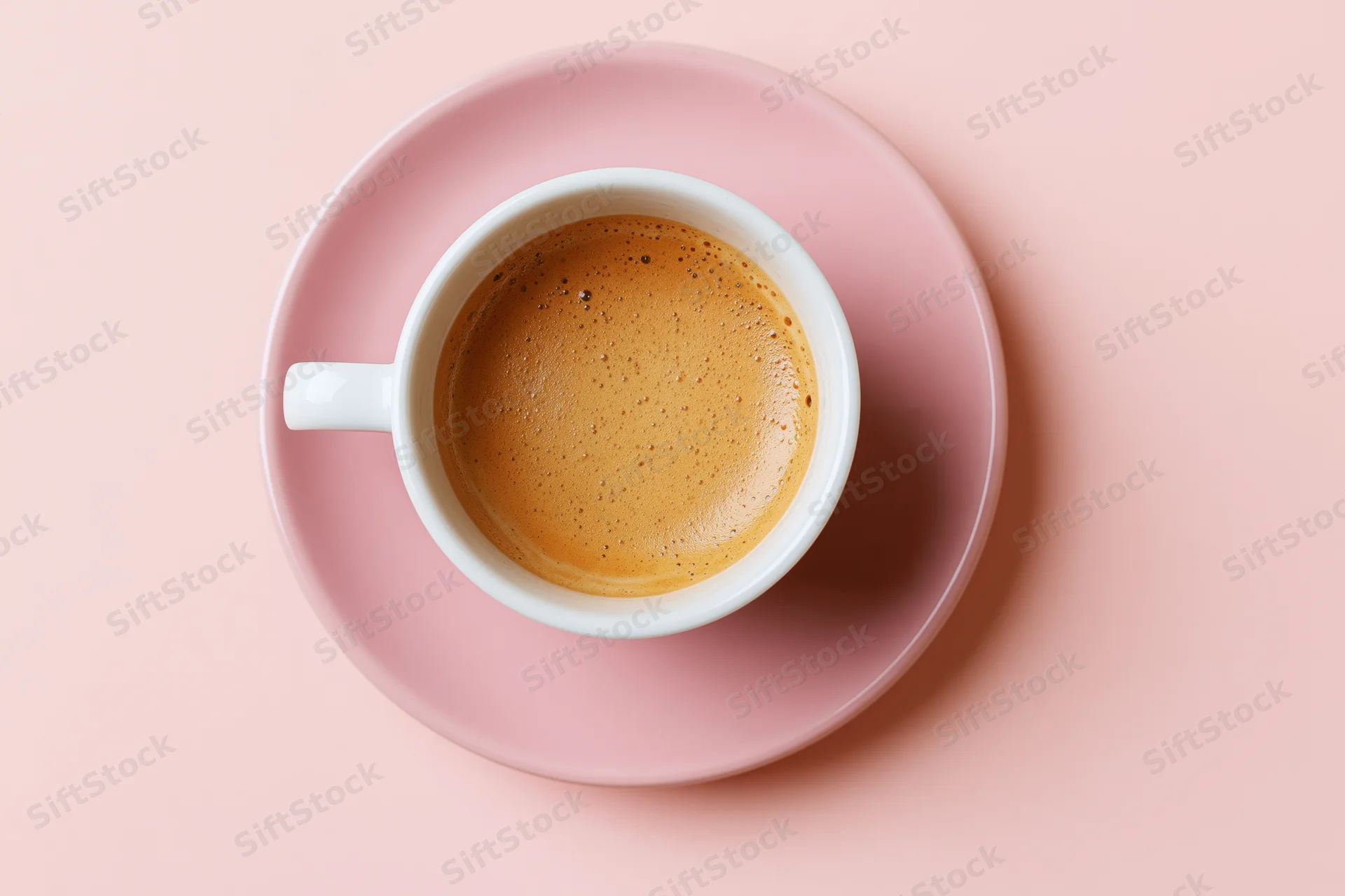 White ceramic coffee cup with frothy espresso on pink saucer, overhead view on pastel background