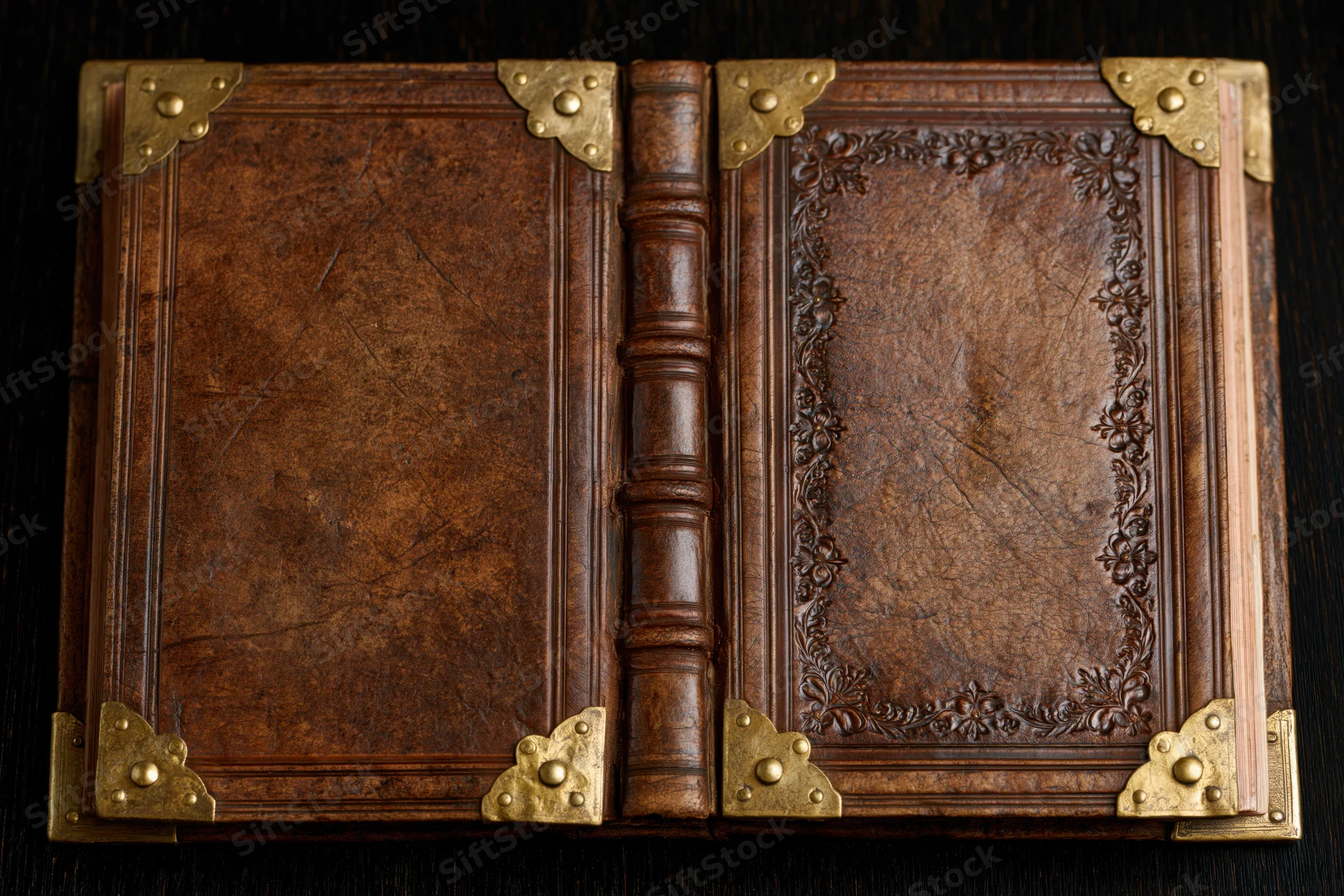 Open antique leather-bound book with brass corners and embossed floral design on dark surface