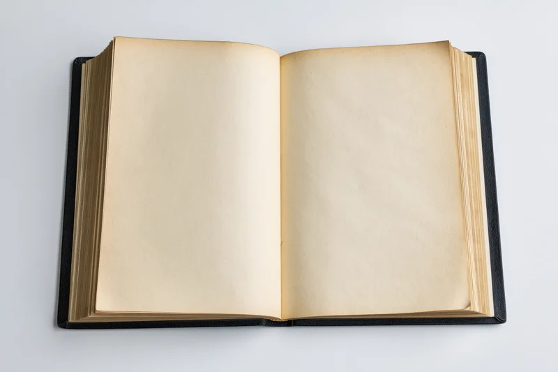 Open hardcover book with blank yellowed pages on white surface