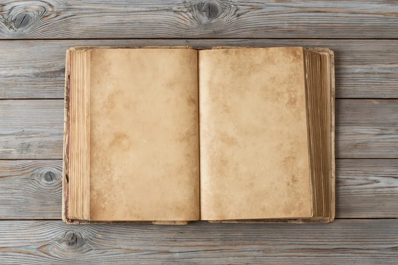 Open vintage hardcover book with blank yellowed pages on a weathered wooden table