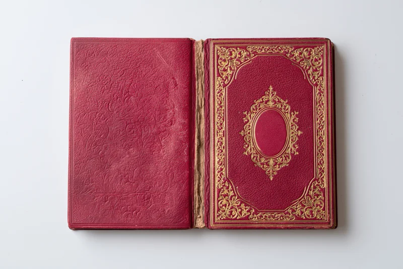 Open antique book with crimson leather covers and gold embossed decoration on white background