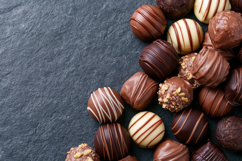 Assorted chocolate pralines and truffles scattered on dark slate surface