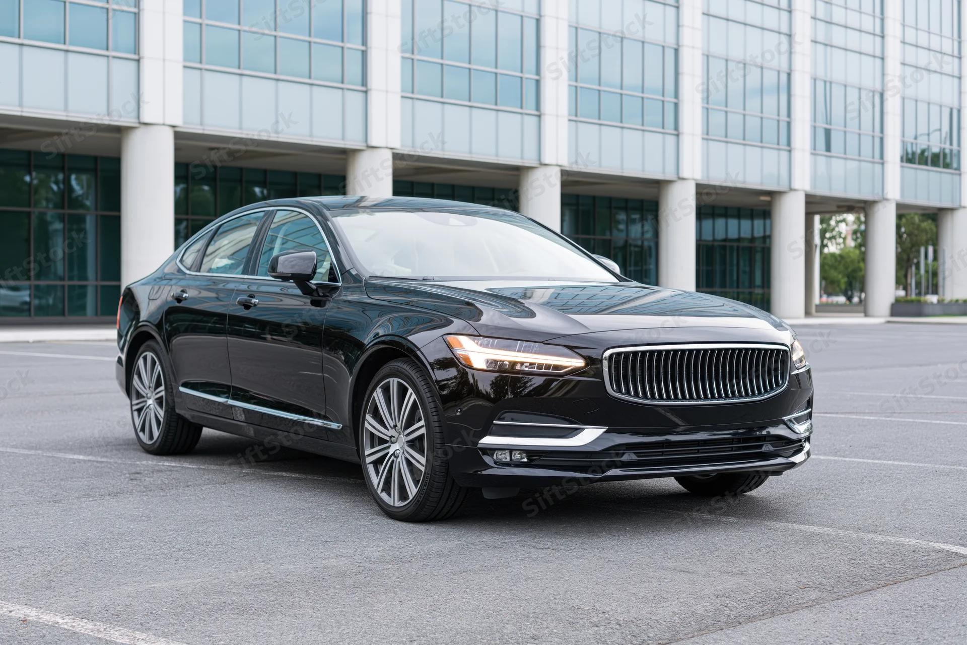 Black luxury executive sedan parked in front of modern office building on asphalt lot