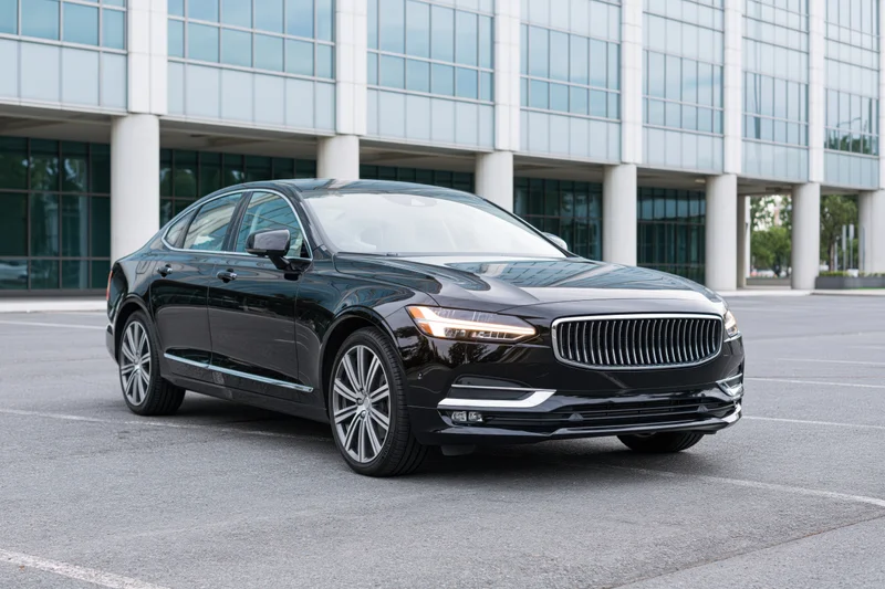 Black luxury executive sedan parked in front of modern office building on asphalt lot