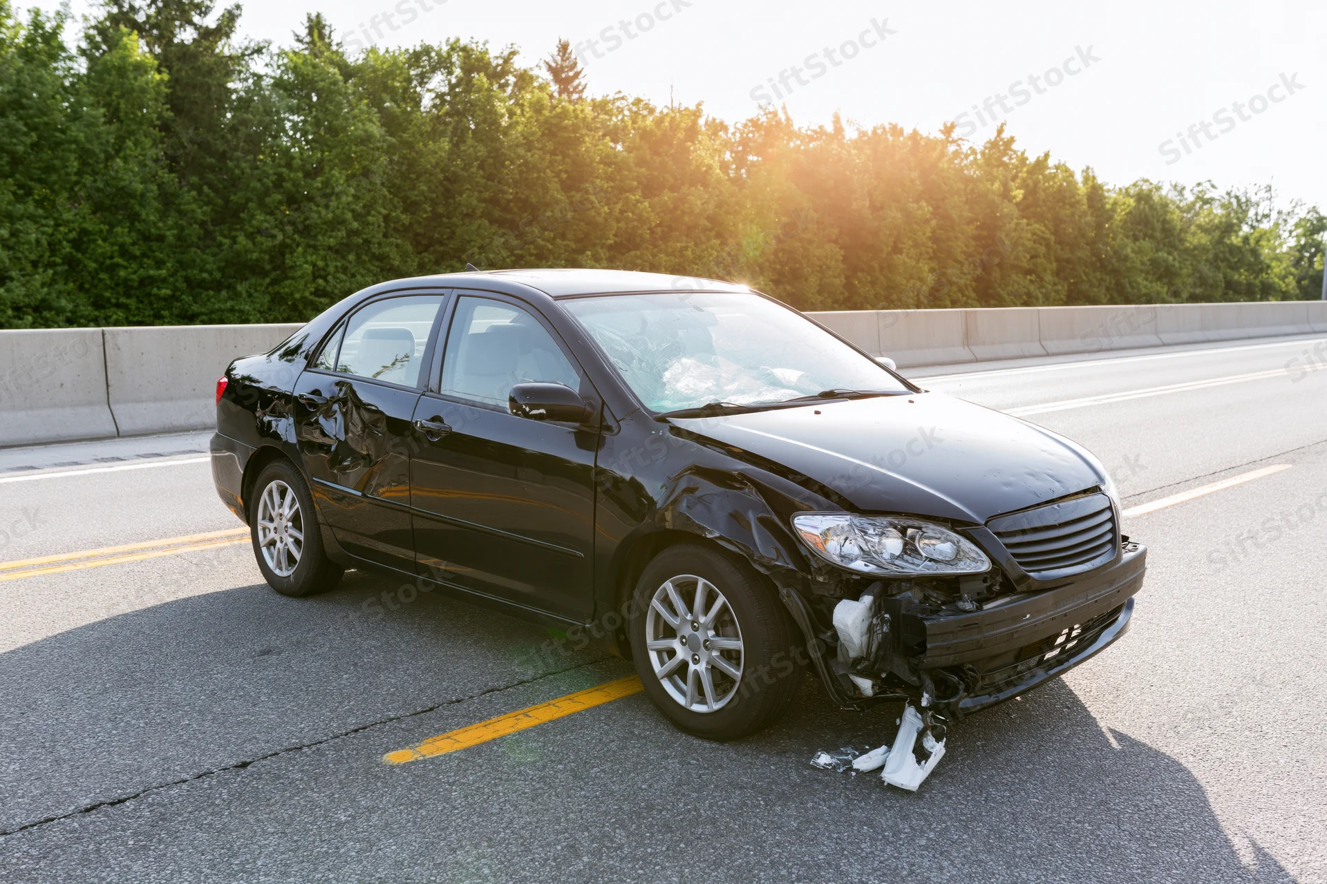 Black sedan with crumpled front end parked on highway shoulder
