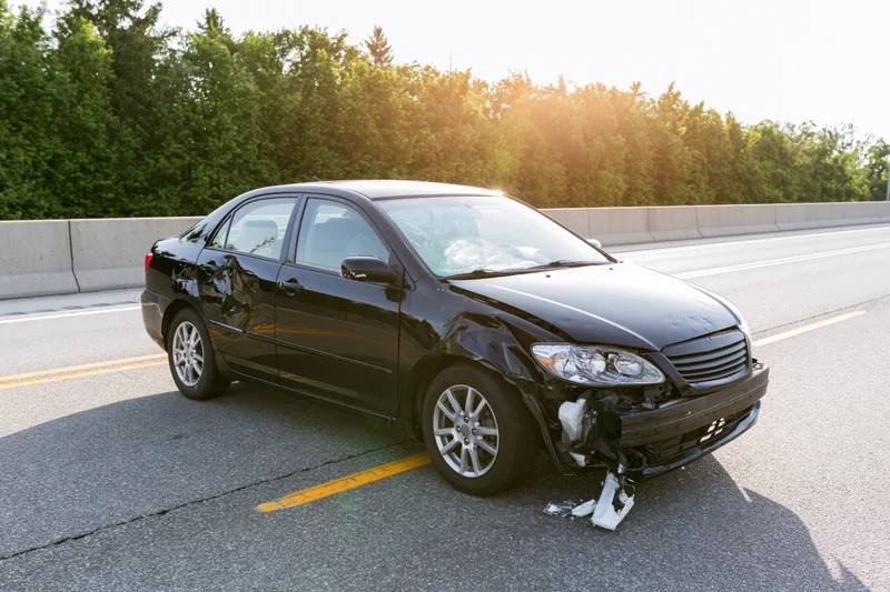 Black sedan with crumpled front end parked on highway shoulder