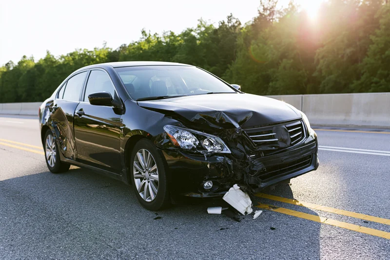 Black sedan with crumpled front end and broken bumper on highway road