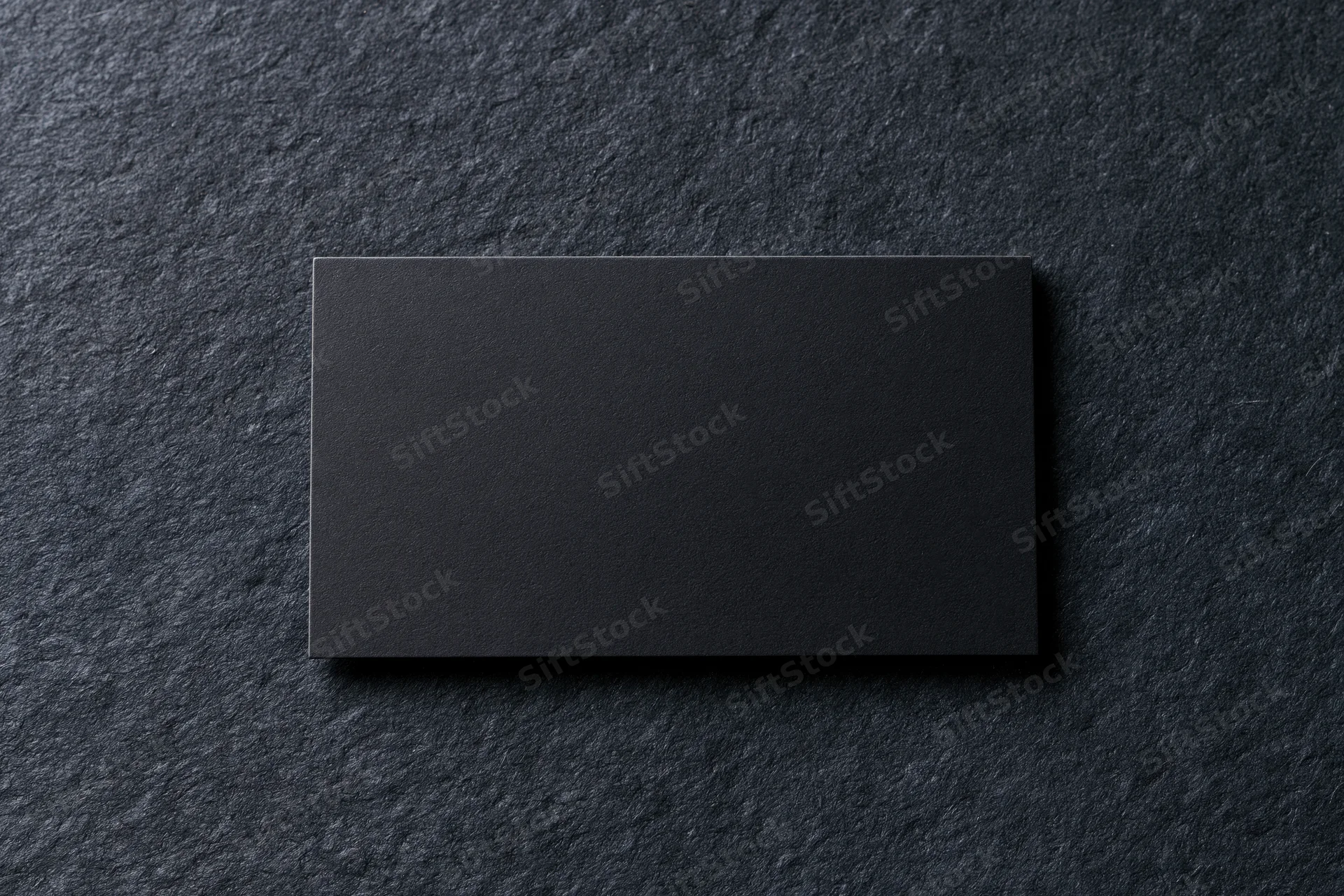 Blank black matte business card lying flat on dark charcoal textured surface