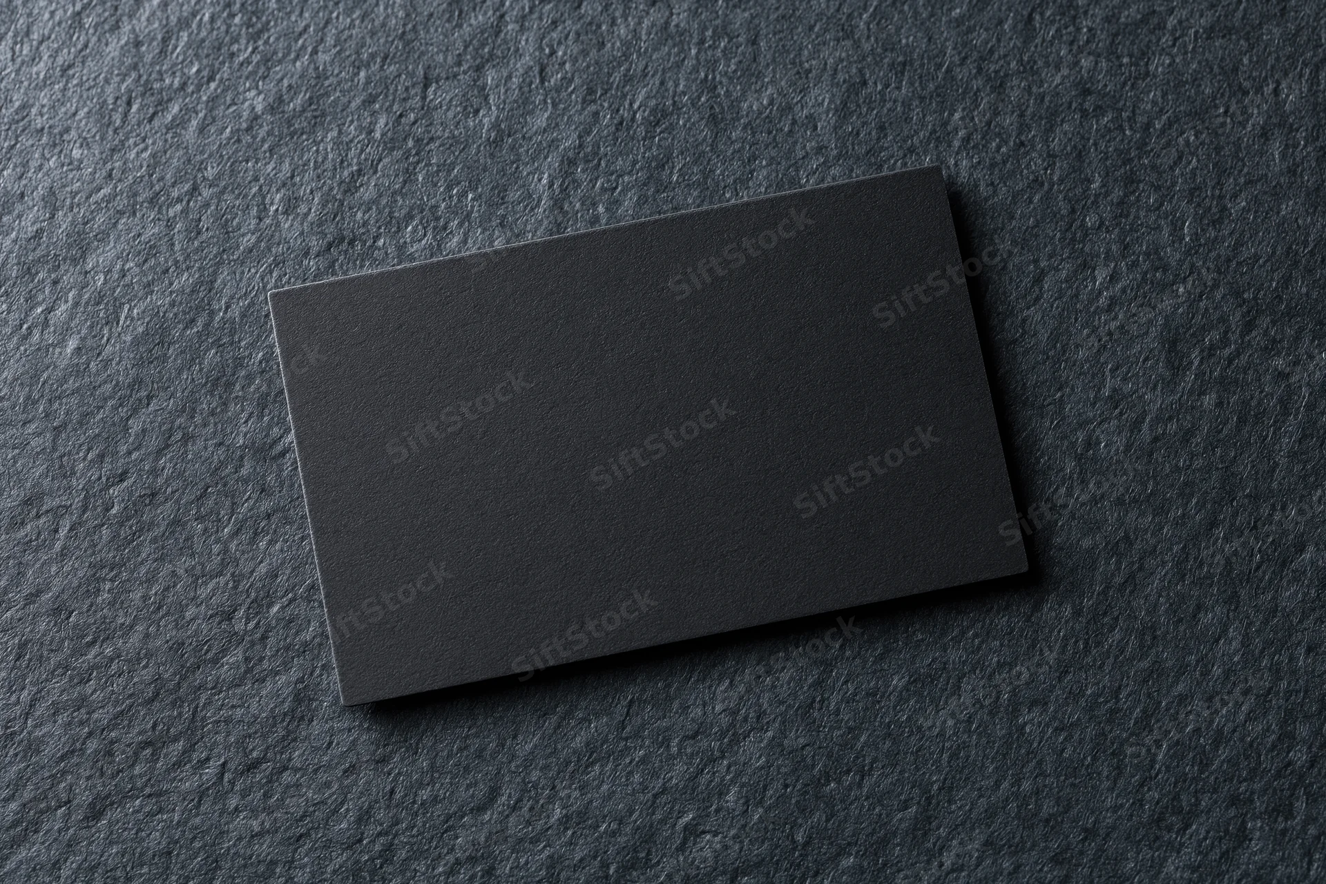 Blank black matte business card lying flat on dark charcoal textured surface