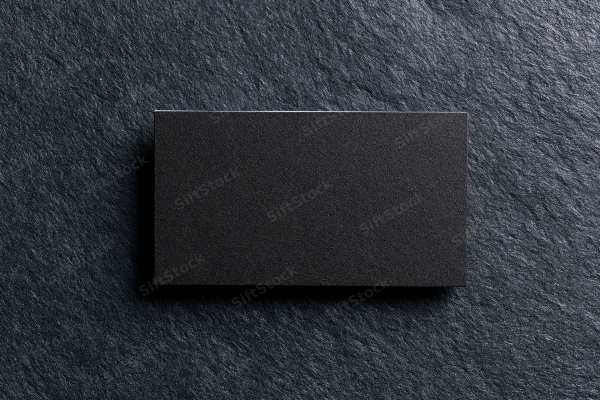 Blank black matte business card lying flat on dark charcoal stone surface