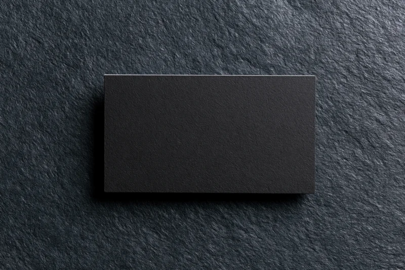Blank black matte business card lying flat on dark charcoal stone surface