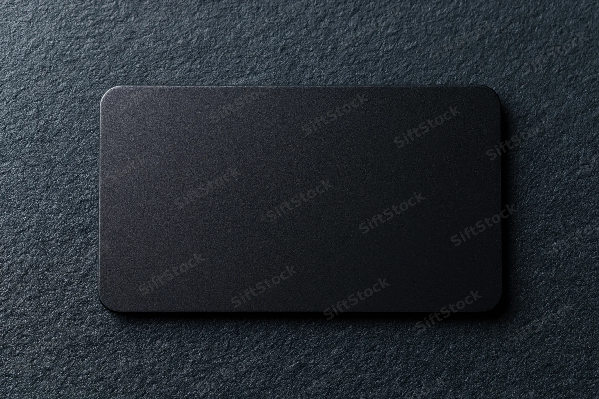 Blank black matte business card lying flat on dark charcoal textured surface
